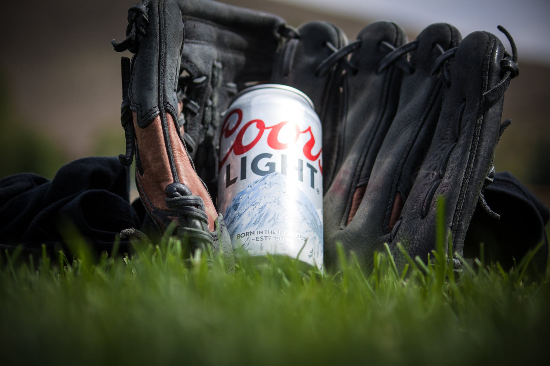 close up photography of coors light beer near black baseball mitts